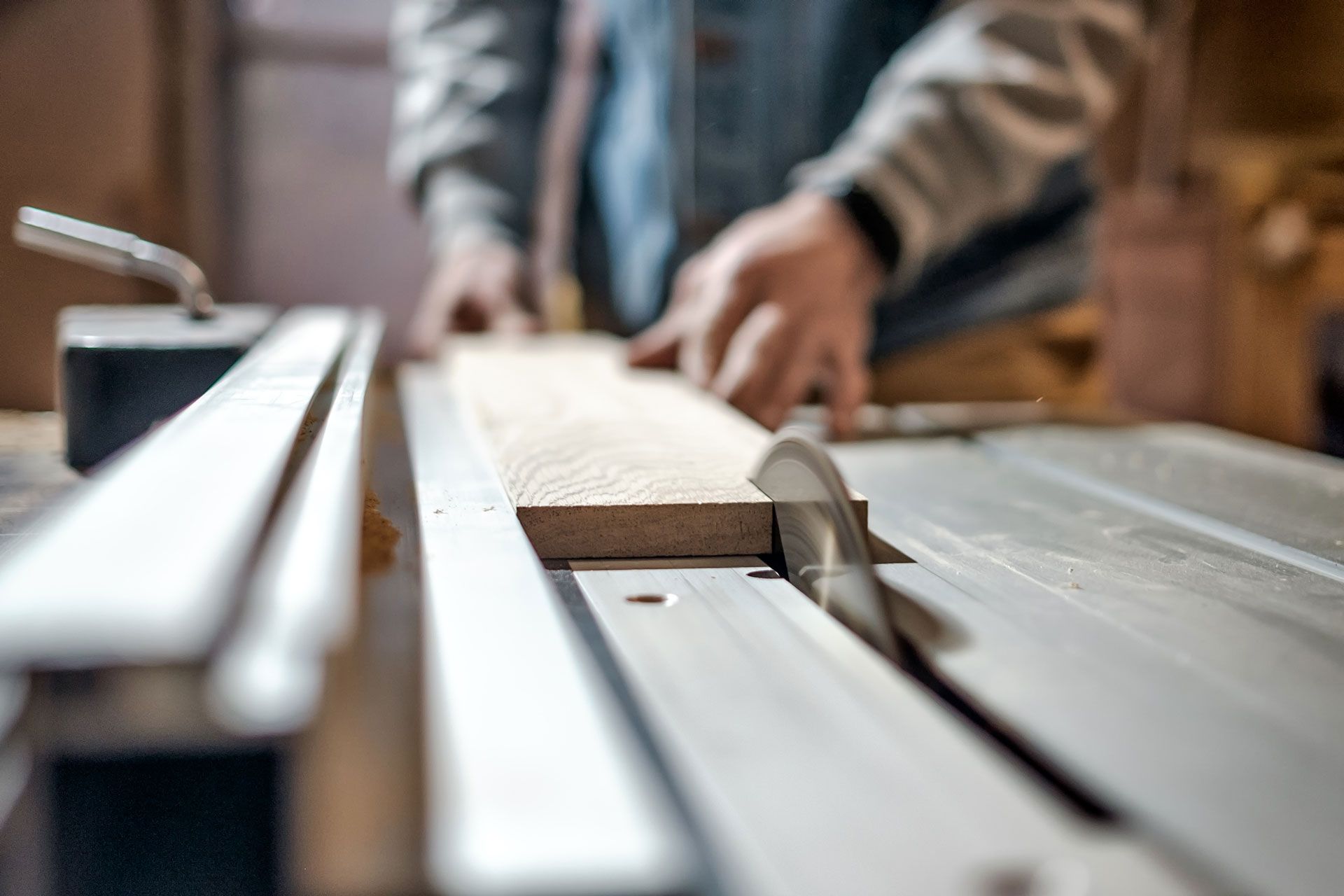 A man is cutting a piece of wood on a table saw.