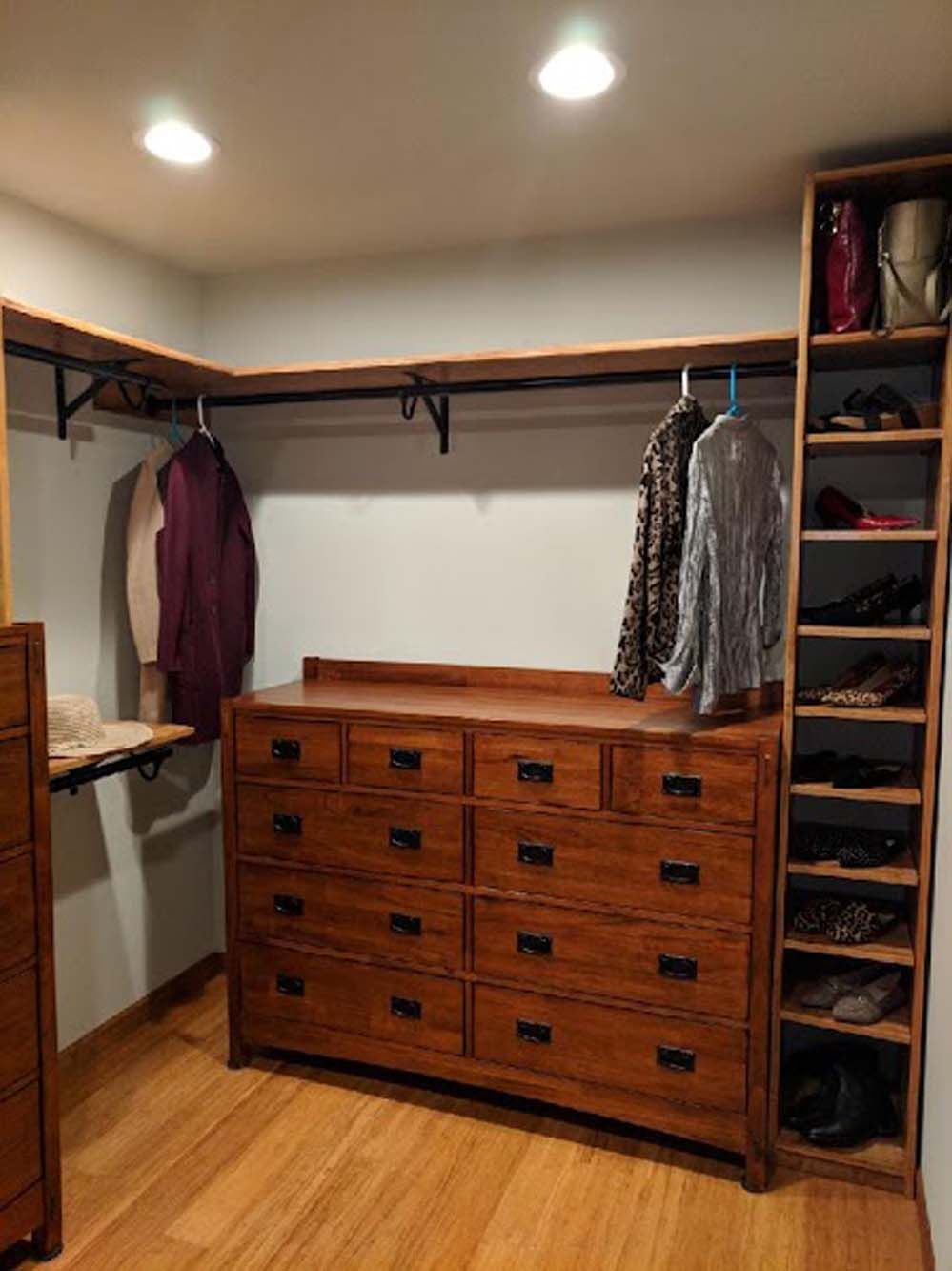 A walk in closet with a dresser and shelves filled with clothes and shoes.