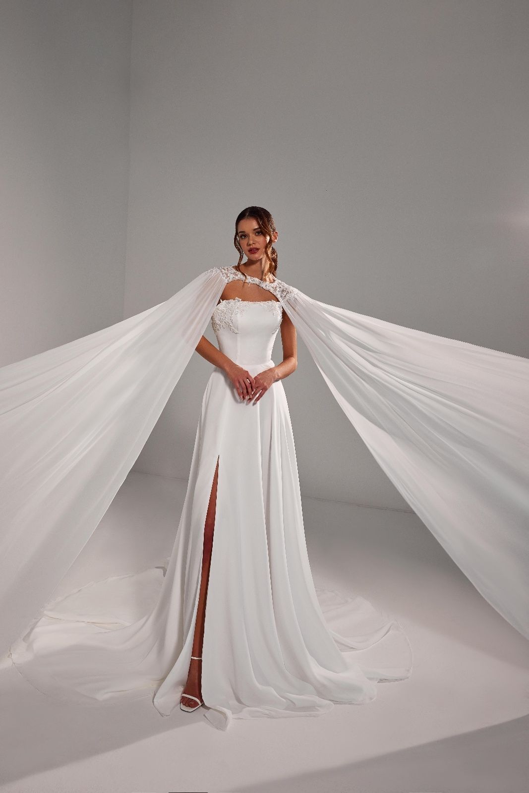 Una donna indossa un abito da sposa bianco con un mantello.