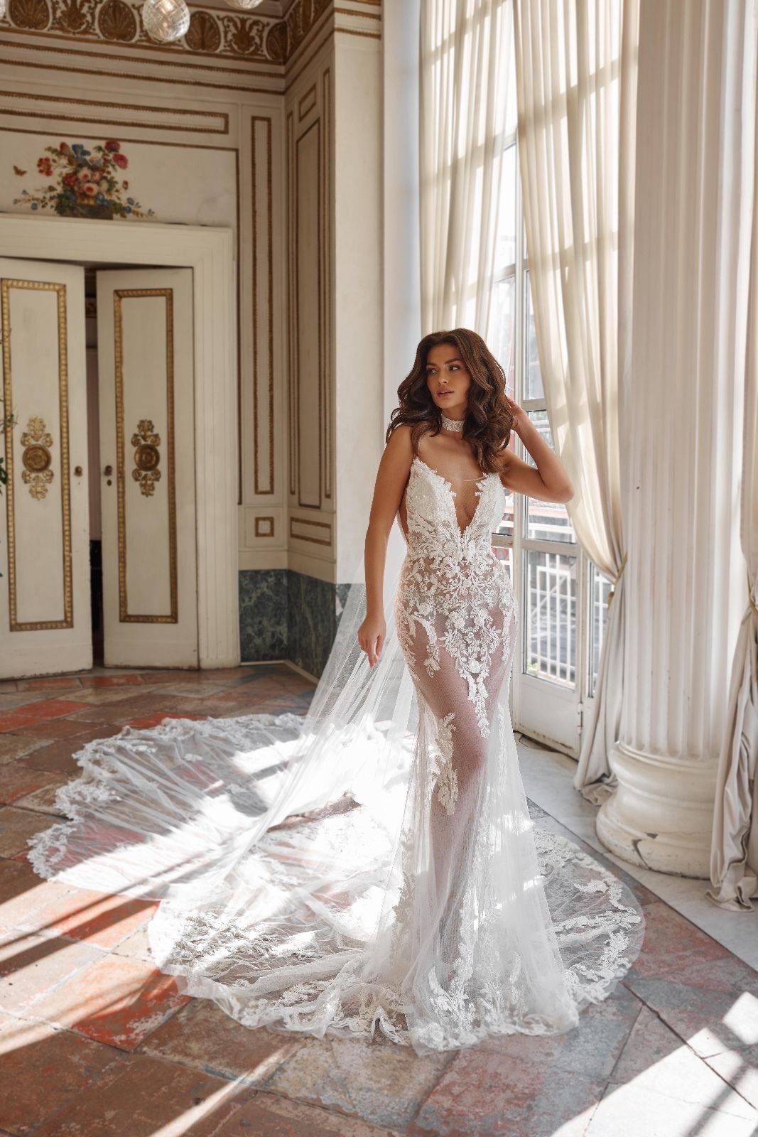 Una donna in abito da sposa è in piedi in una stanza accanto a una finestra.