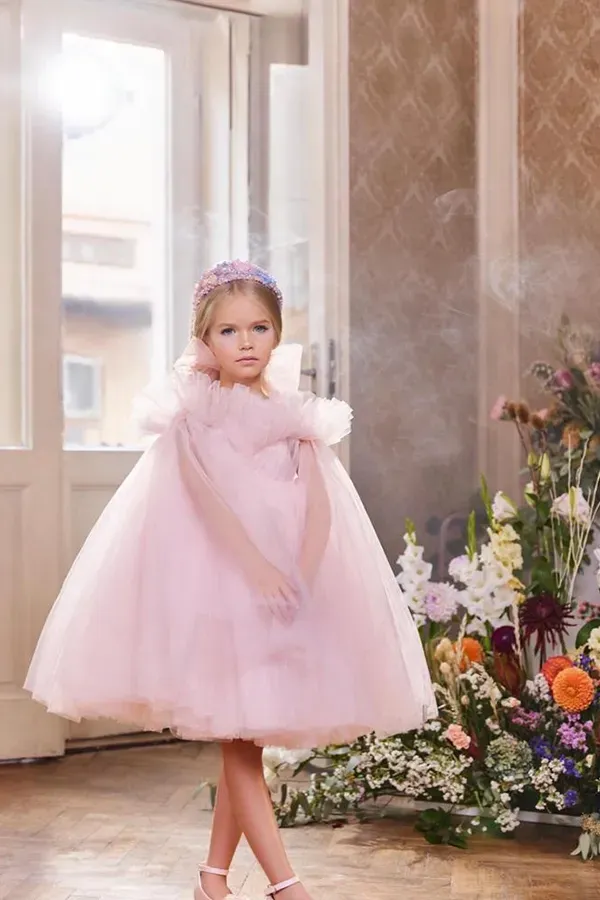 Una bambina con un vestito rosa è in piedi in una stanza piena di fiori.