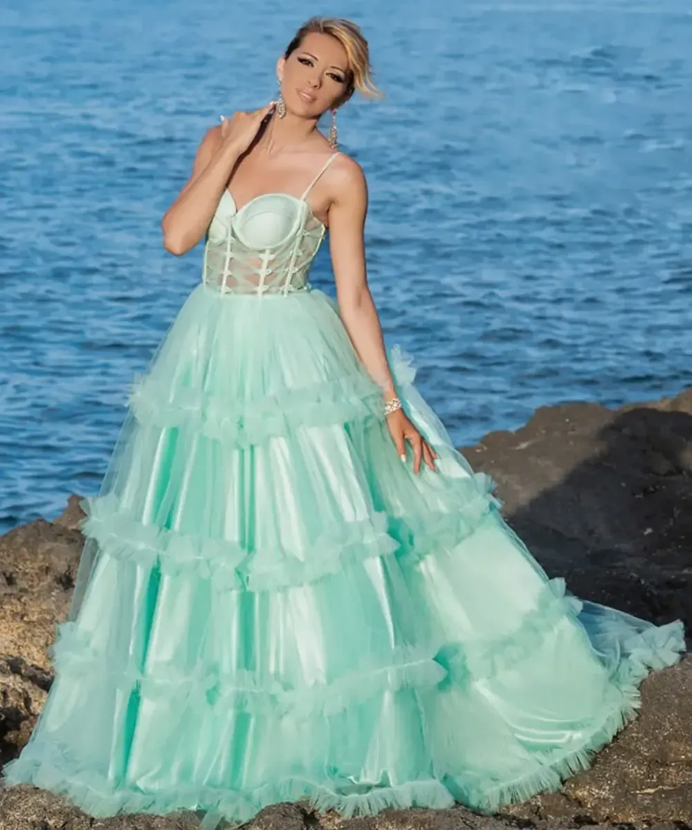 Una donna con un lungo abito verde è in piedi su una roccia vicino all'oceano.