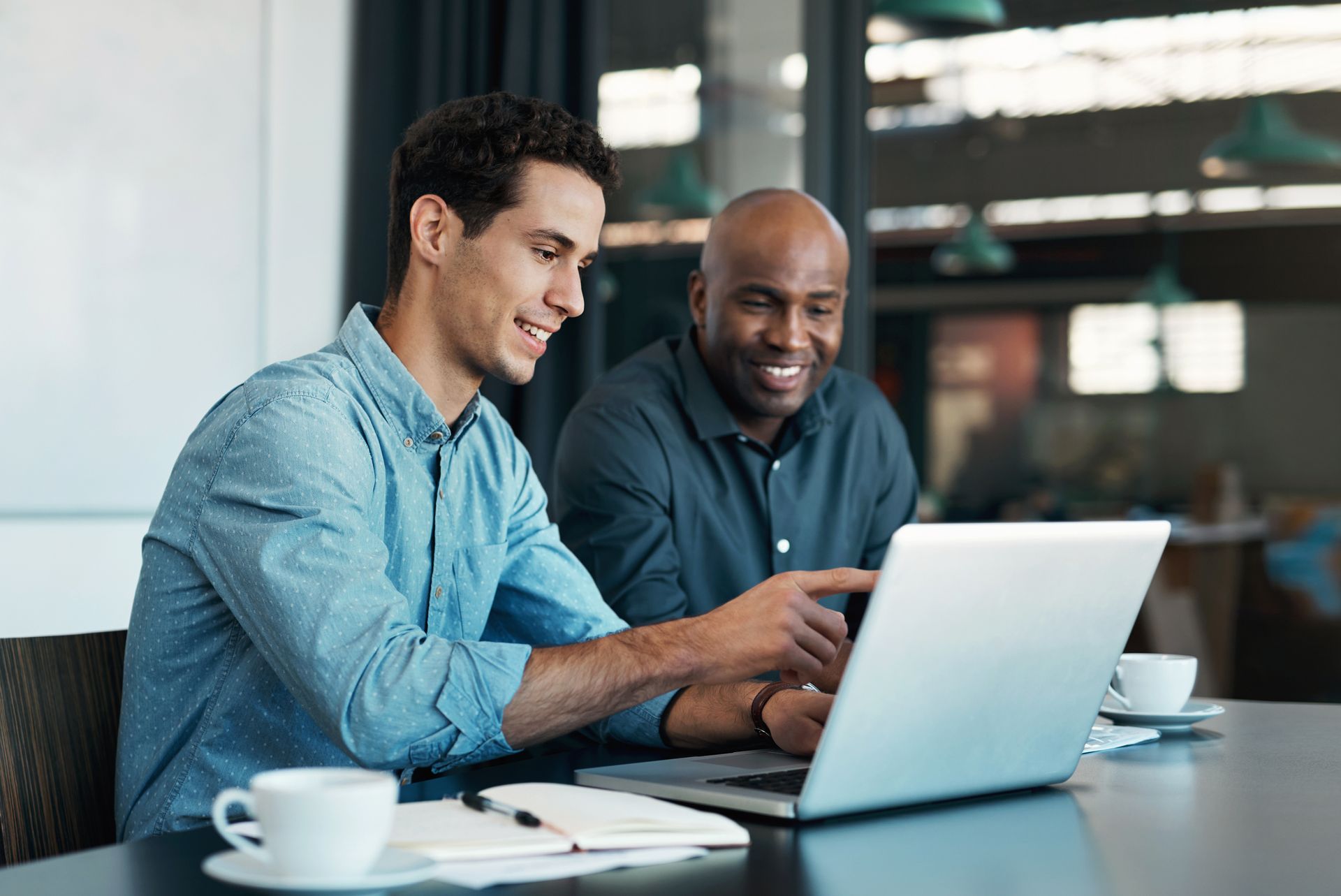 Two men are sitting at a table looking at a laptop computer.