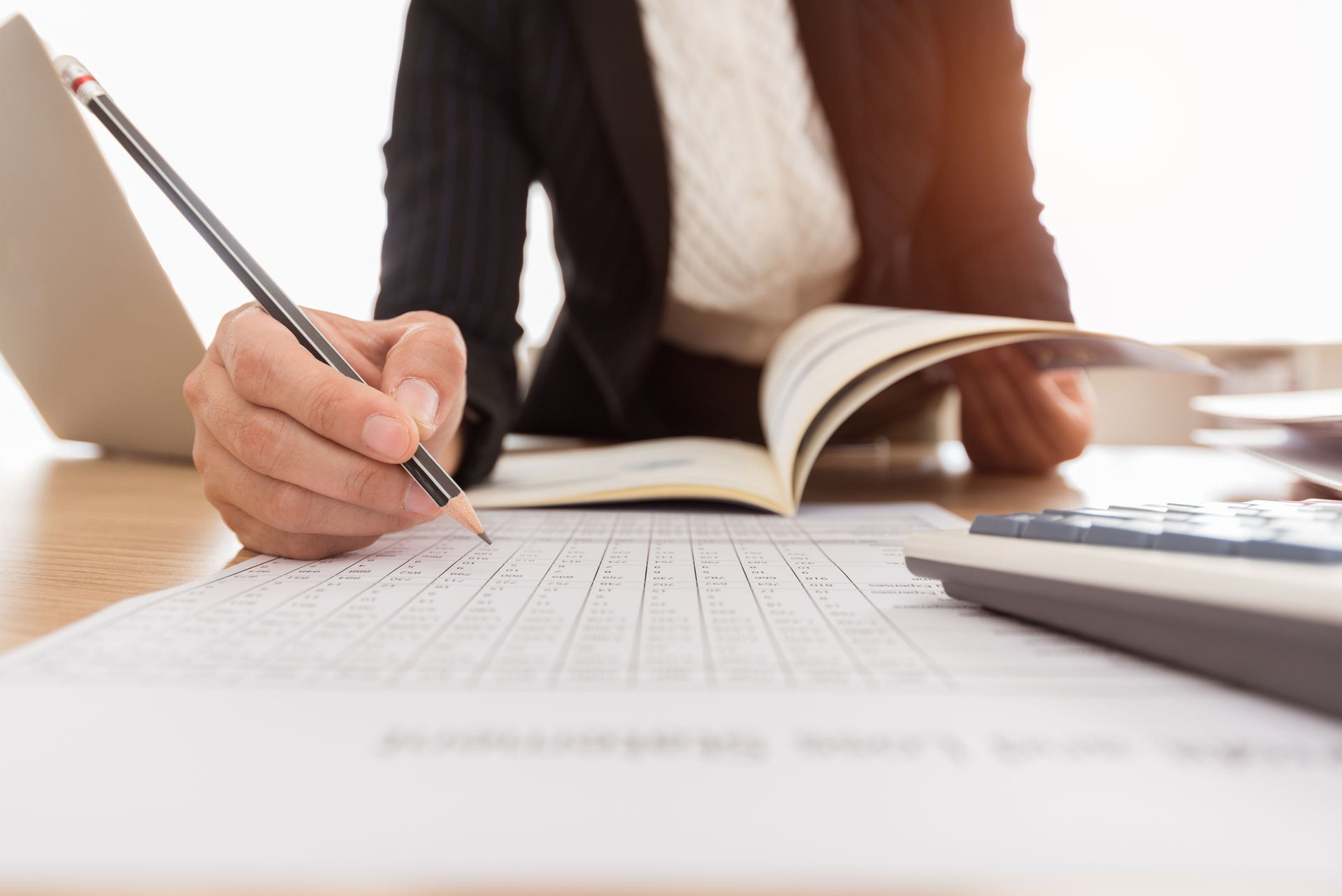 A woman is sitting at a desk holding a pencil and writing on a piece of paper.