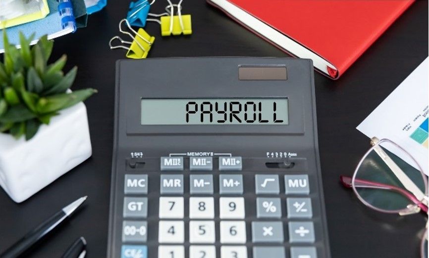 Payroll Services concept with calculator displaying 'Payroll', pen, and documents on dark desk.