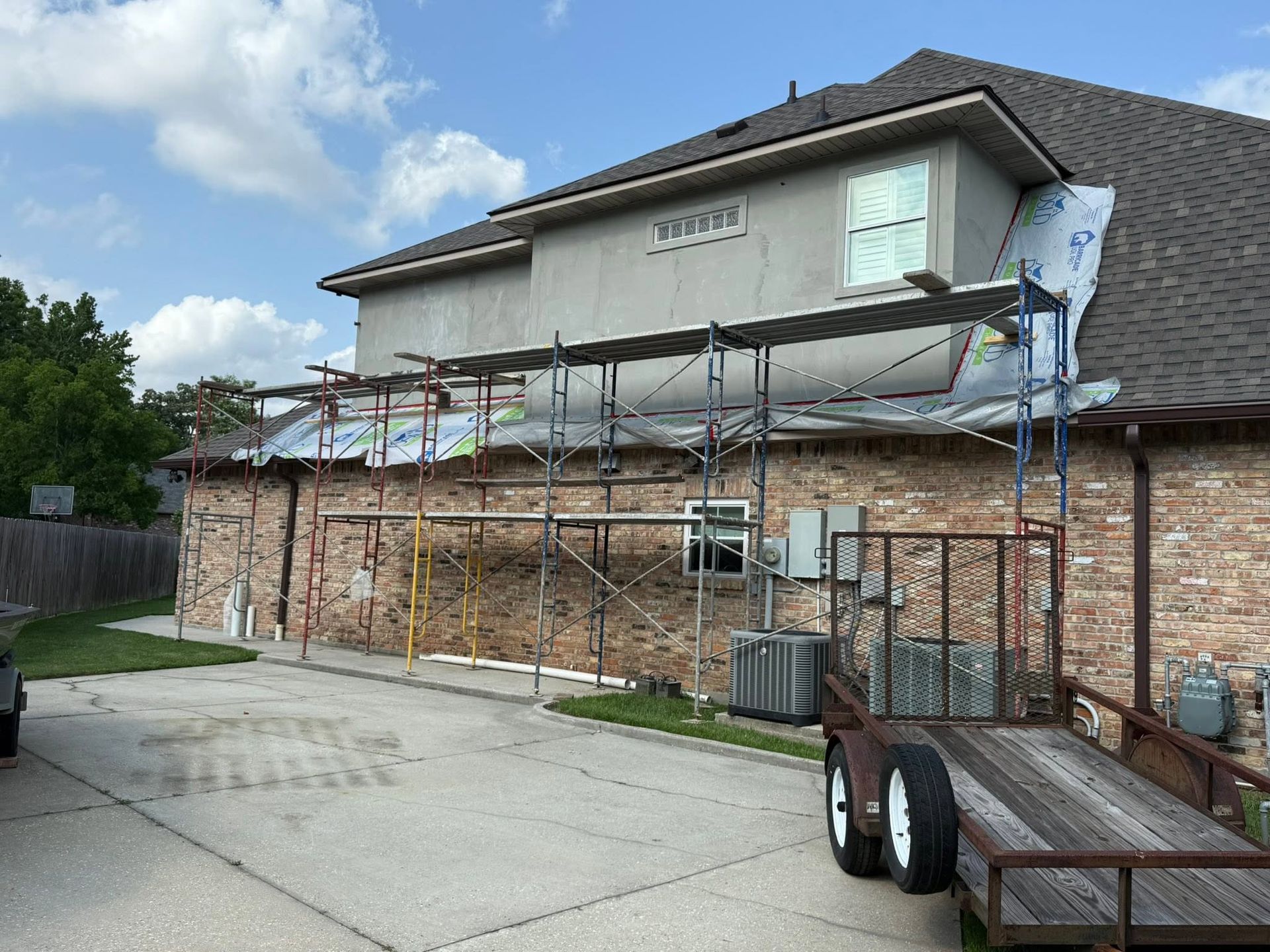 House exterior with scaffolding and roof repair work over a brick garage and driveway.