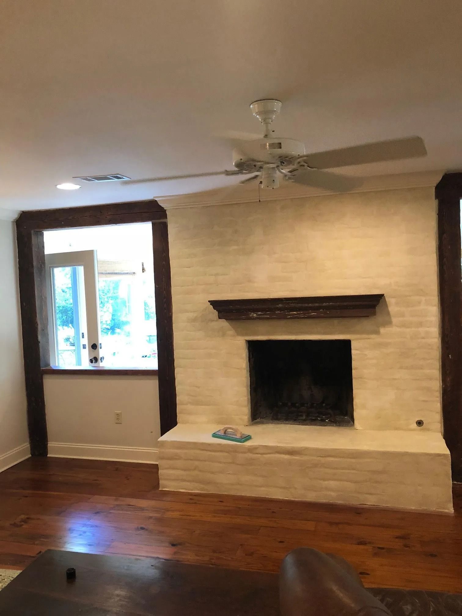 Empty living room with brick fireplace, window, ceiling fan, and hardwood floors