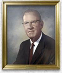 Portrait of a man in a suit, glasses, and a red tie, framed in gold.