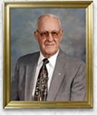 Portrait of an older man in a suit and tie, smiling, framed in gold.