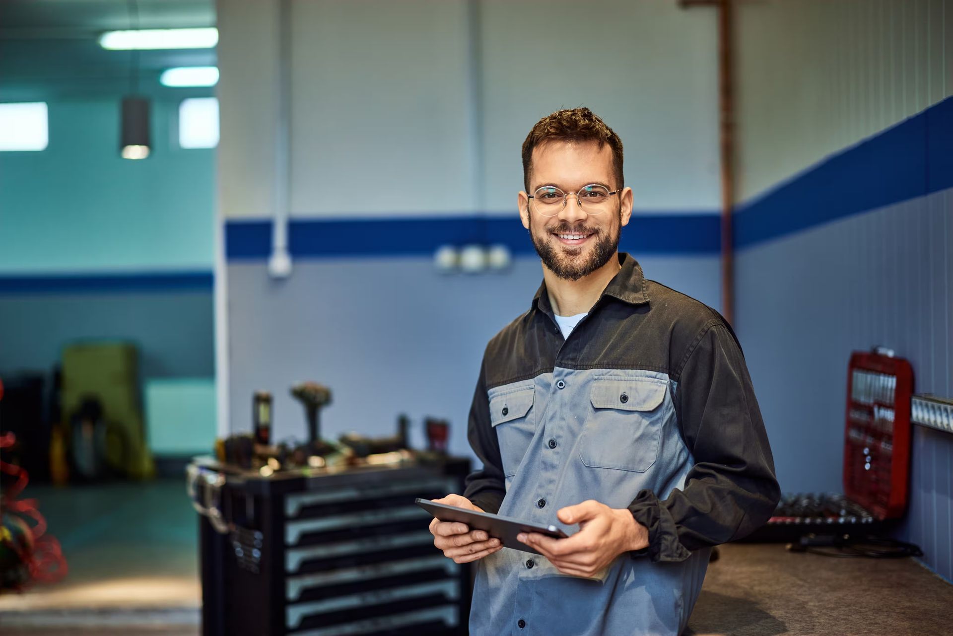 Mechanic holding tablet, smiling in auto shop.