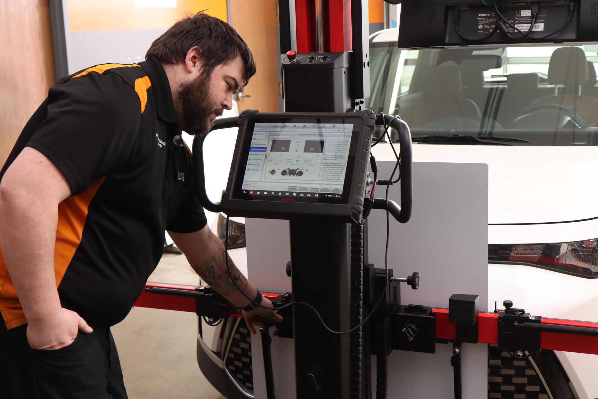 Mechanic using a diagnostic tool to align a vehicle's wheels in a garage setting.