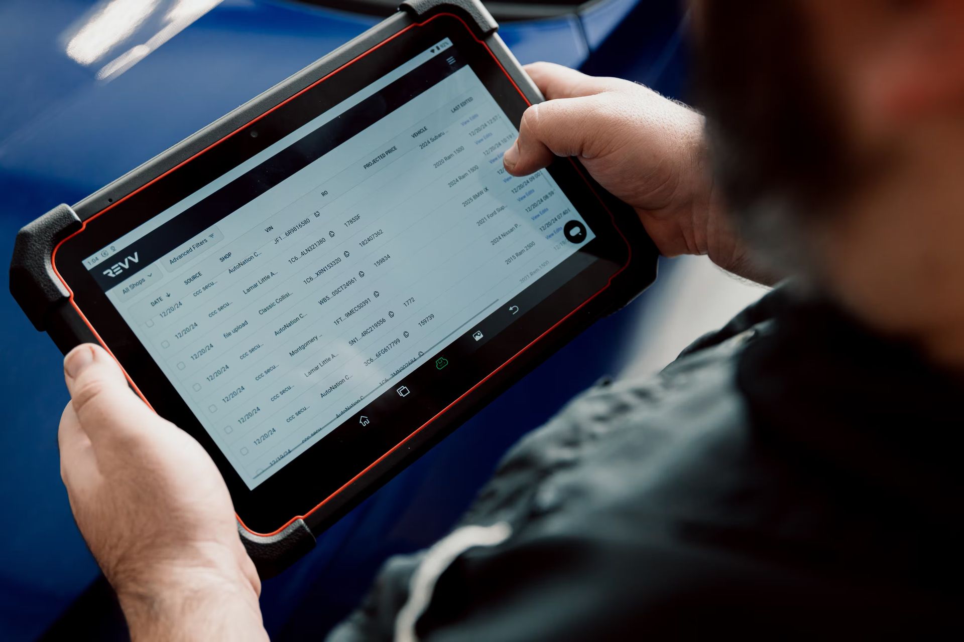 Person using a tablet computer to view data, likely for automotive diagnostics, near a blue car.