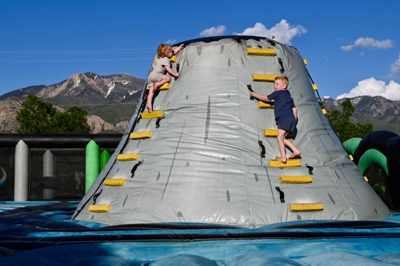 A boy and a girl are playing on an inflatable volcano.