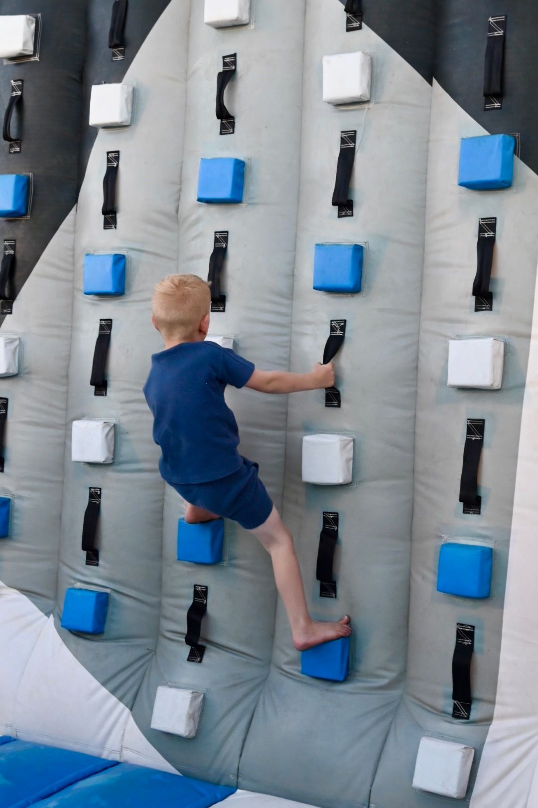A young boy is climbing up a climbing wall.