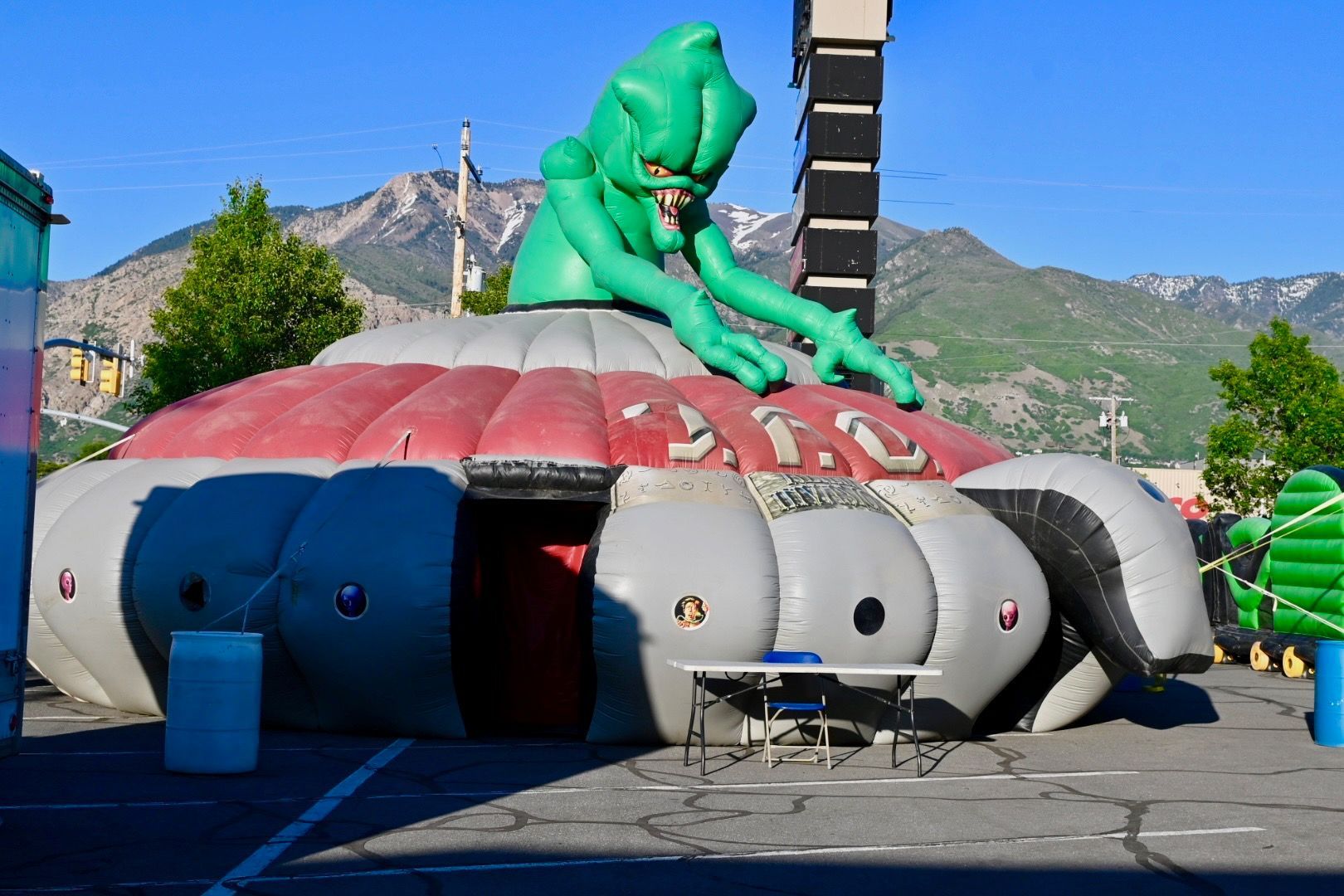A large inflatable alien is sitting on top of a building in a parking lot.