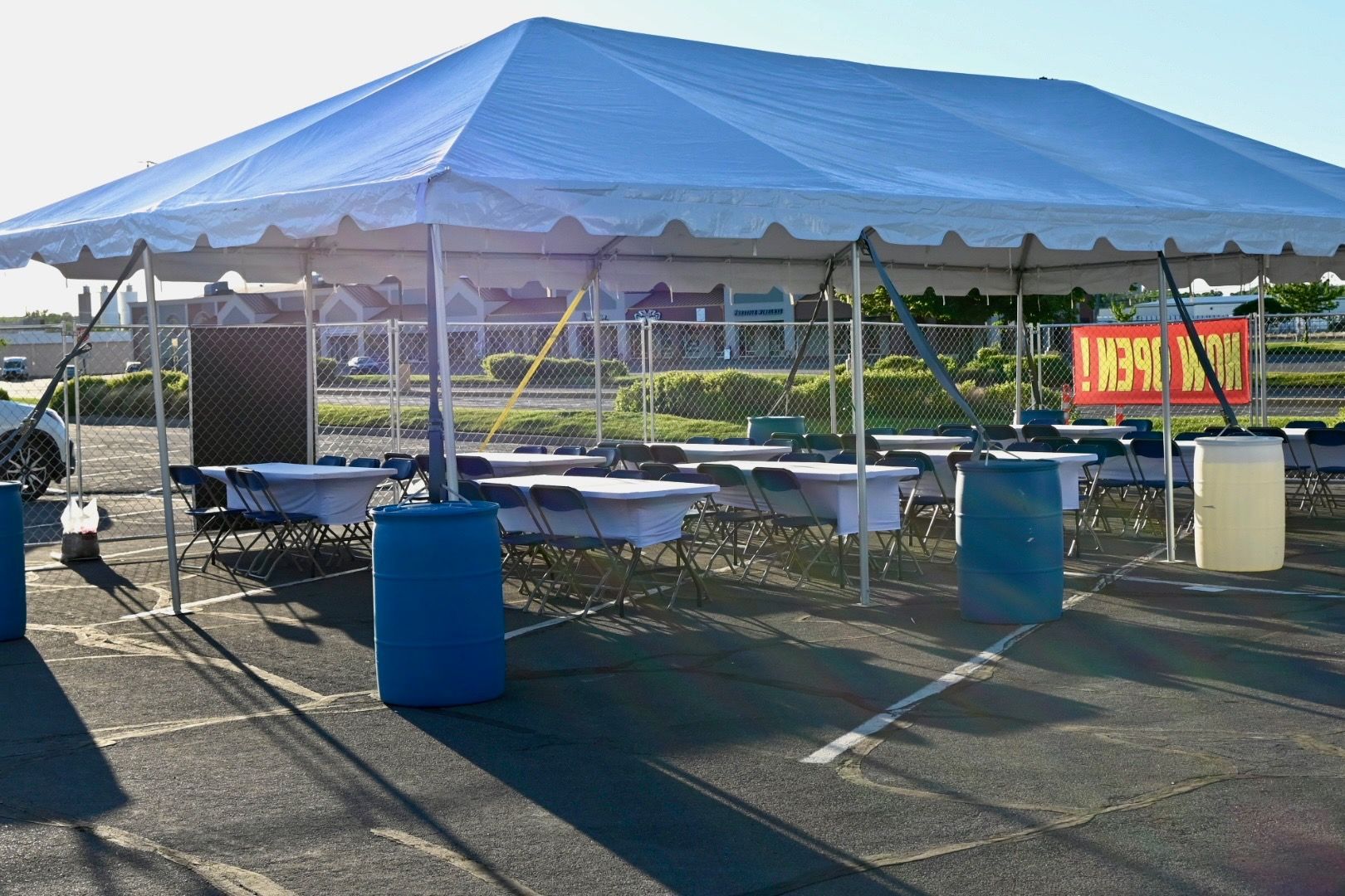 A large blue tent in a parking lot with tables and chairs underneath it