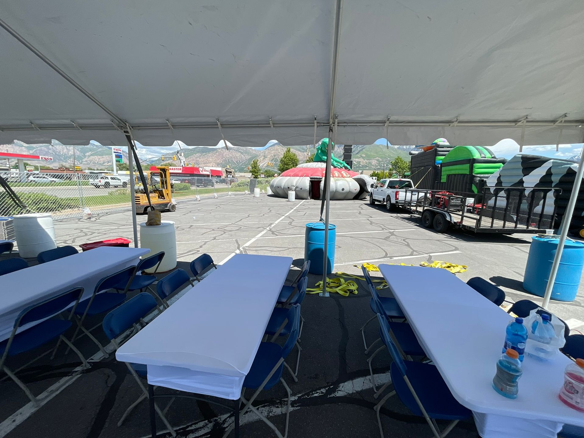 A group of tables and chairs under a tent in a parking lot.