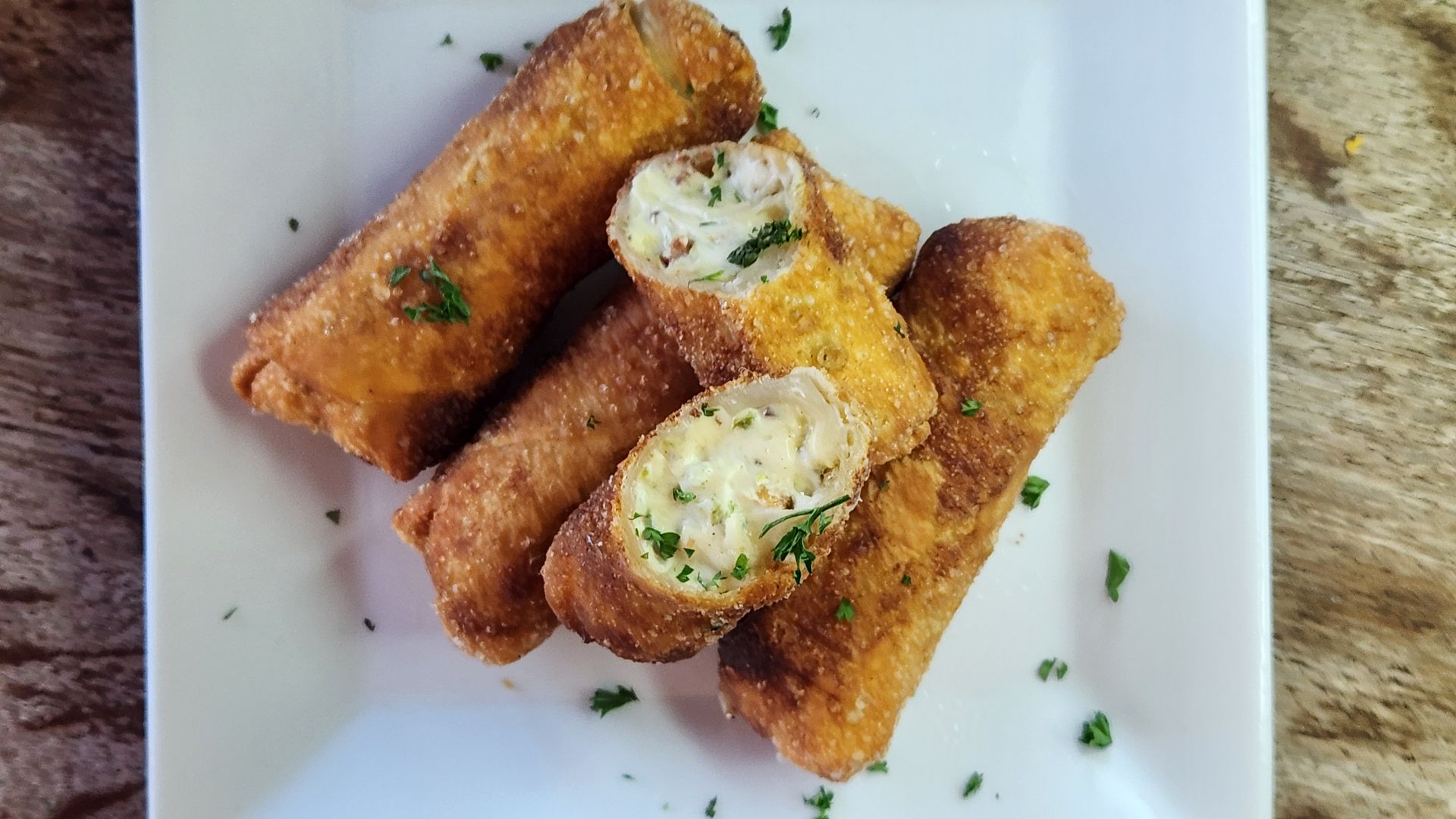 Fried rolls on a white plate, golden-brown exterior, cut open to show cheesy filling, sprinkled with parsley.