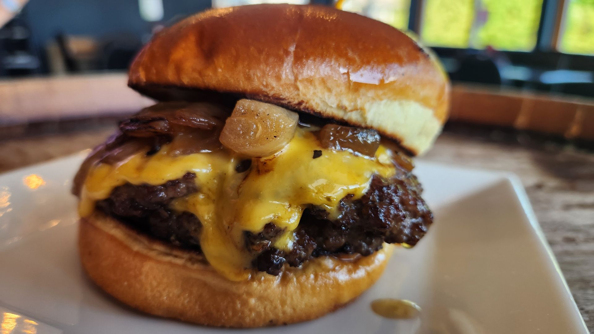 Burger on a white plate; beef patty with melted cheddar, caramelized onions, and a brioche bun.