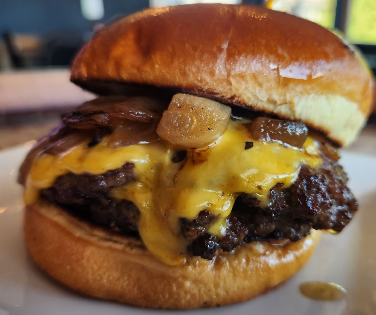 Cheeseburger on a brioche bun with caramelized onions; melted cheese oozing.