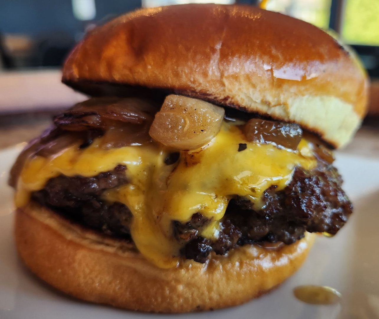 Cheeseburger on a brioche bun with caramelized onions; yellow cheese oozes.