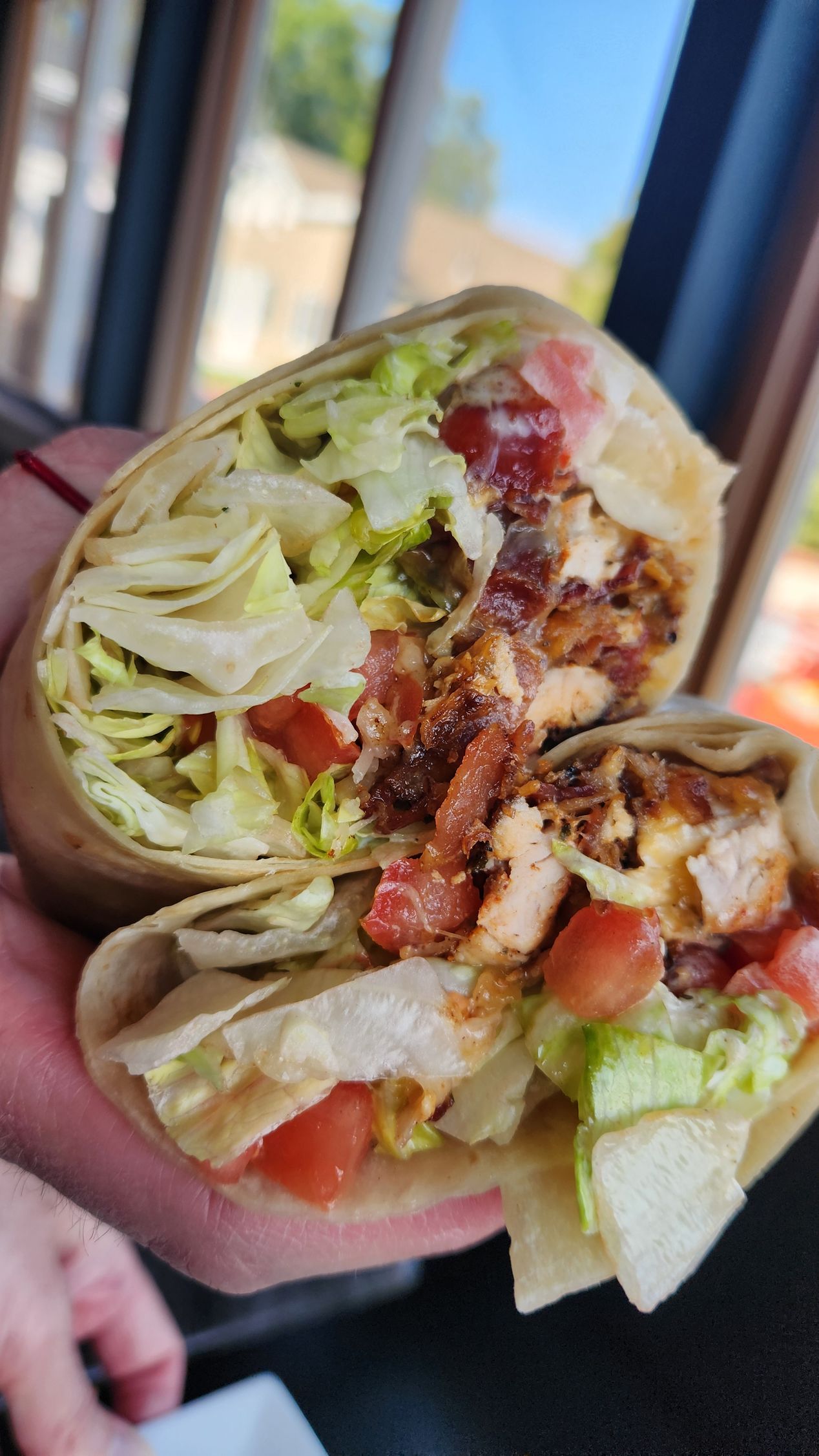 Chicken wrap cut in half, filled with lettuce, tomato, and sauce. Held by hands.