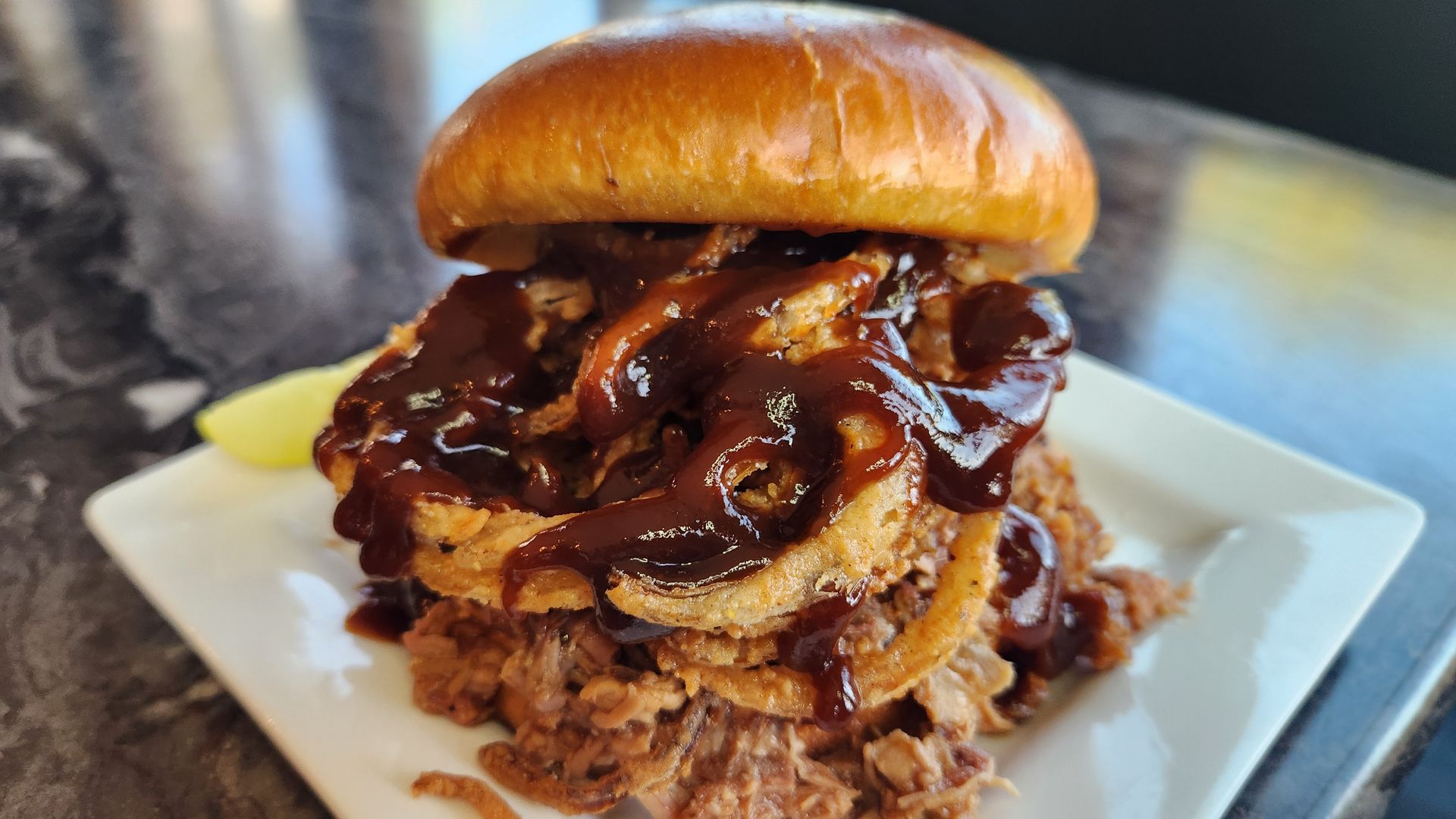 Burger with fried onion rings, BBQ sauce, and a brioche bun on a plate.