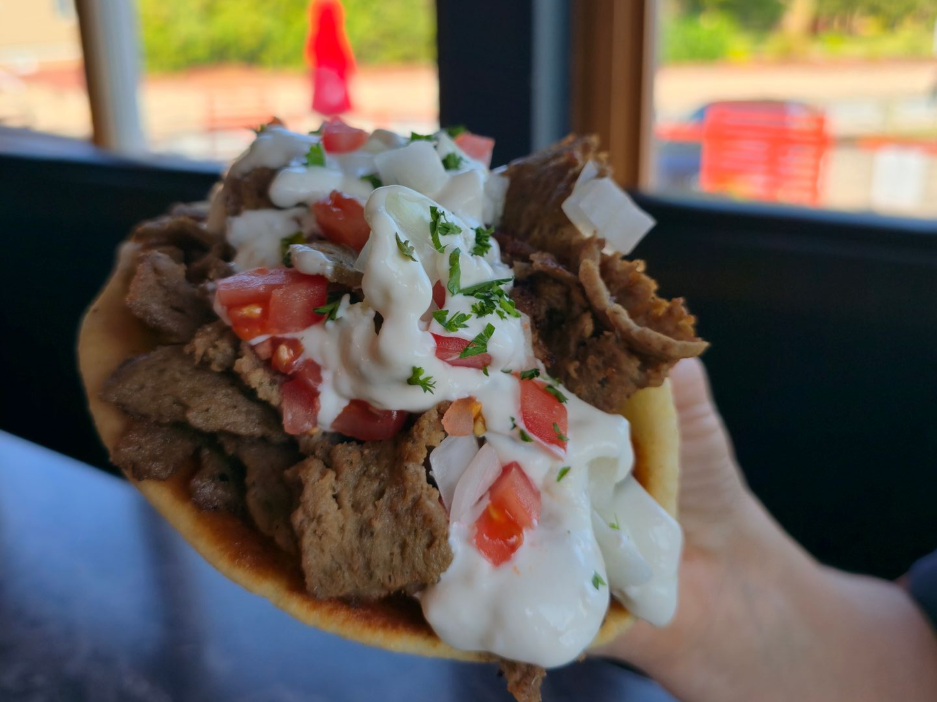 Gyros sandwich with meat, tzatziki sauce, tomatoes, and herbs, held in hand.