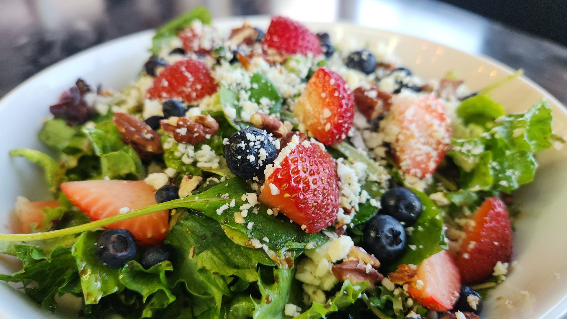 Salad with strawberries, blueberries, pecans, and cheese in a white bowl.