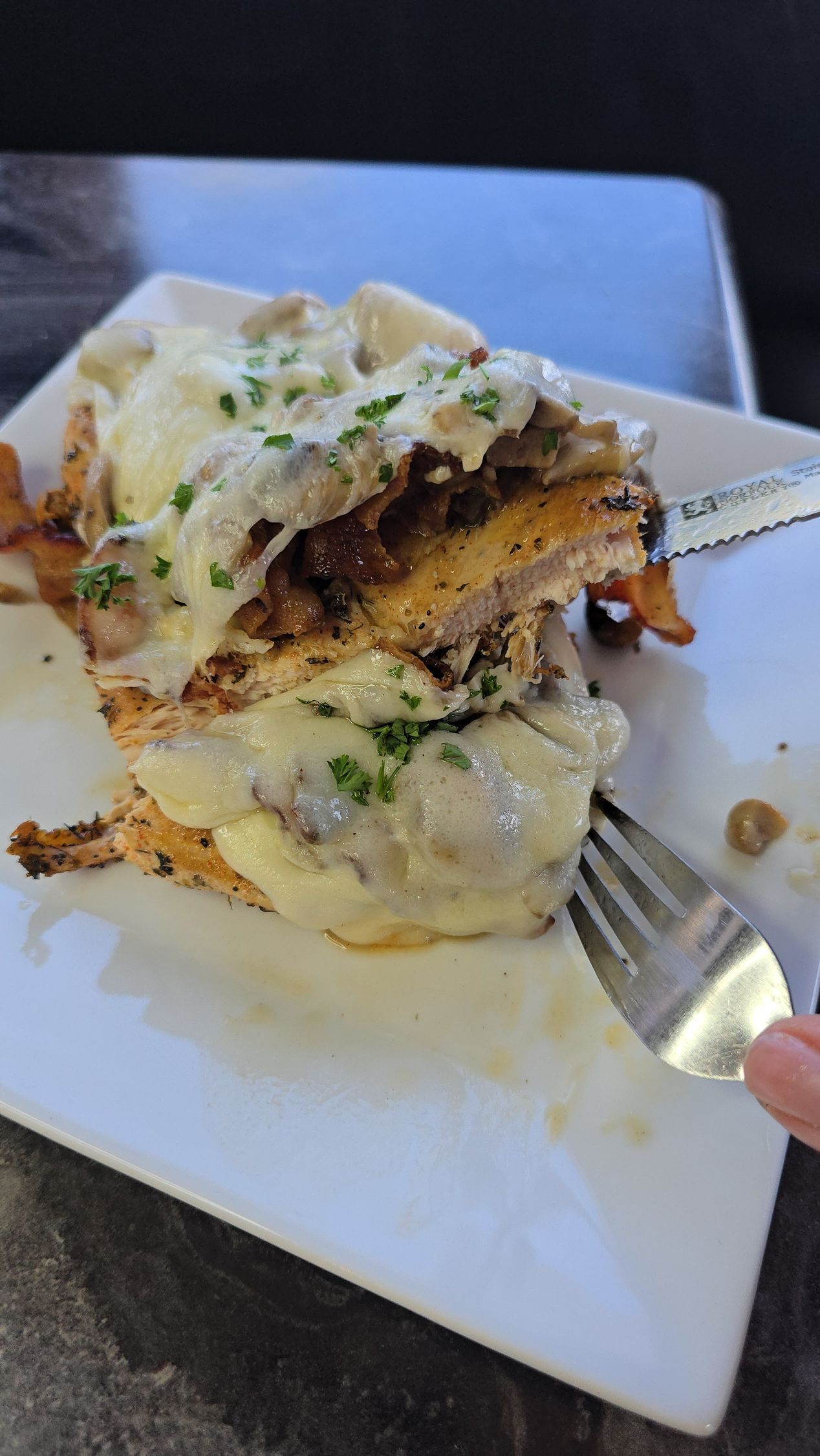 Stacked chicken dish with sauce and mushrooms on a white plate; a fork is being used to eat it.