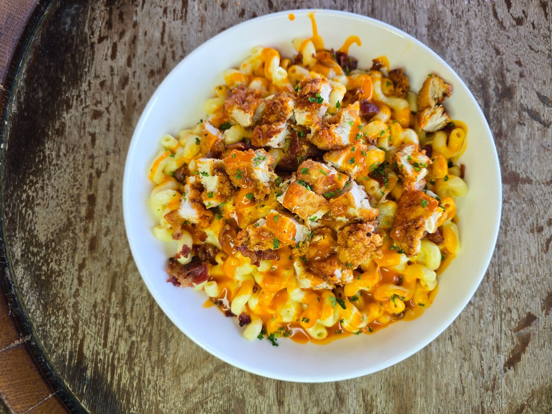 Mac and cheese with diced, breaded chicken in a white bowl on a wooden surface.