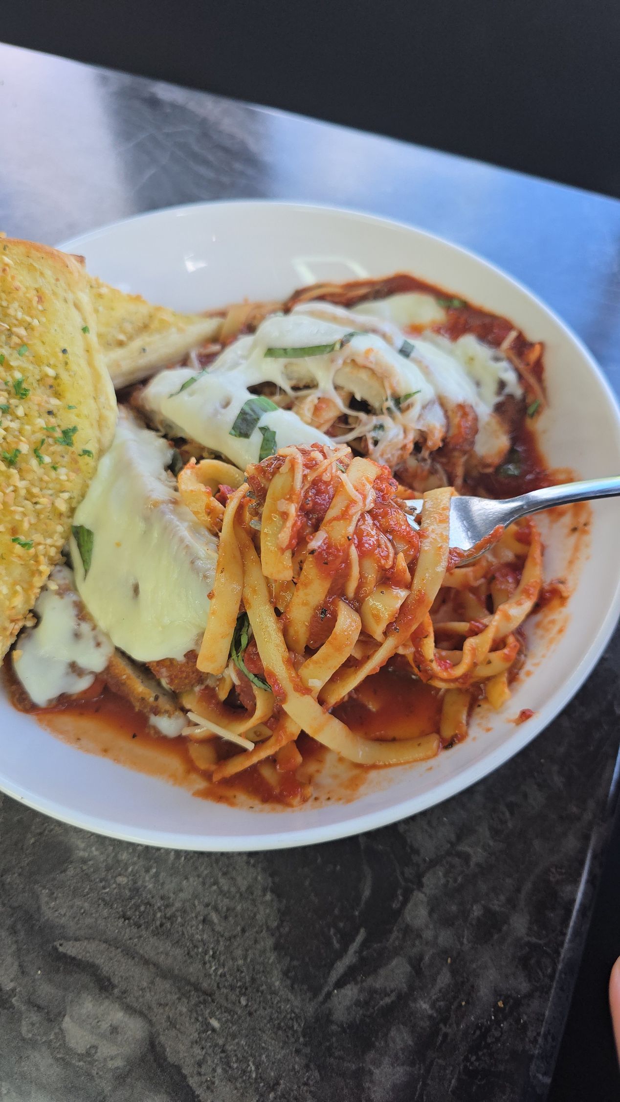 Plate of pasta with red sauce, chicken parmesan, and garlic bread.