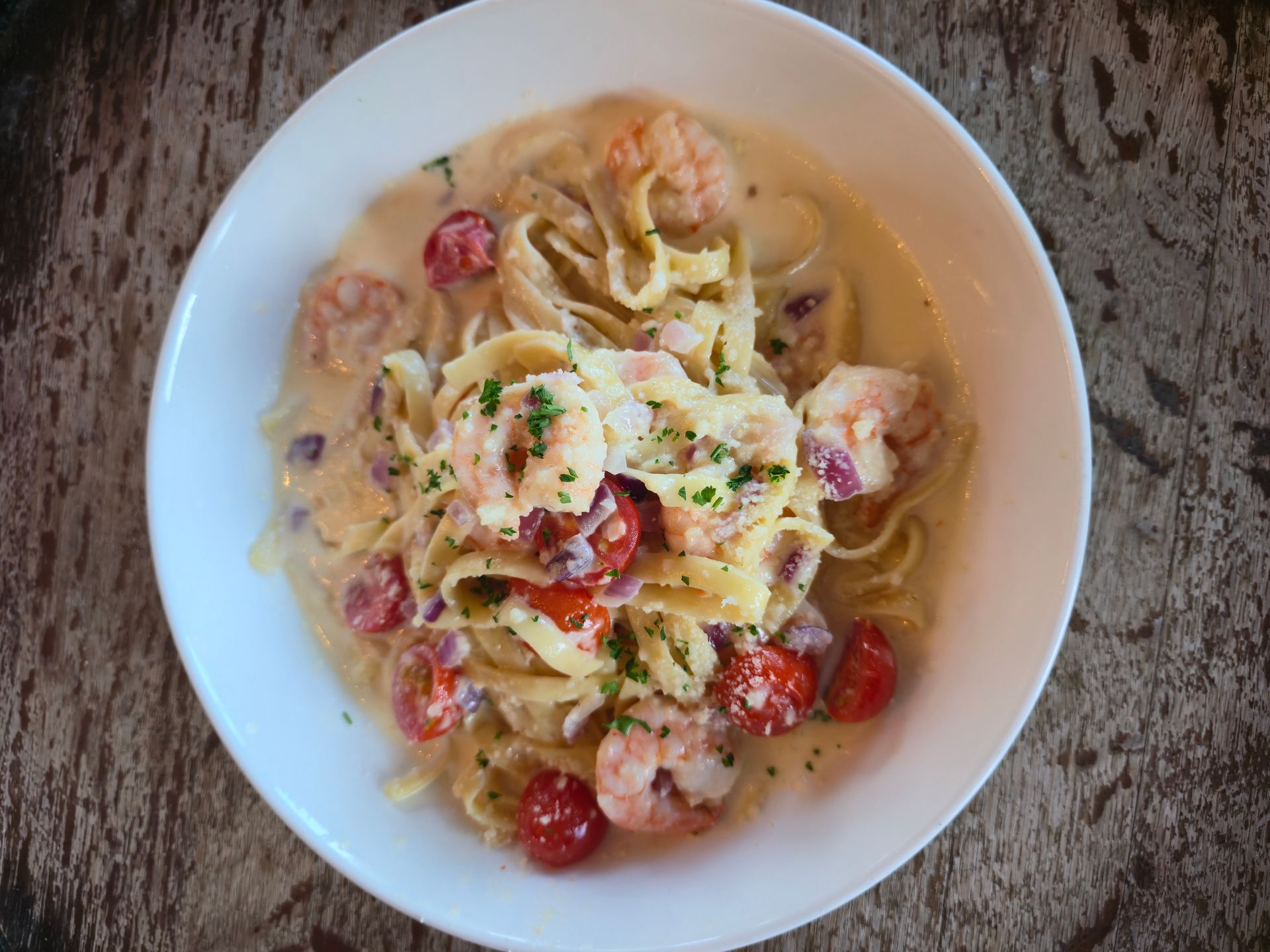 Pasta dish with shrimp, cherry tomatoes, and creamy sauce in a white bowl.