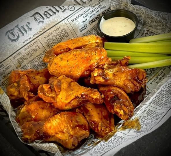 Chicken wings with dipping sauce and celery sticks on newspaper.