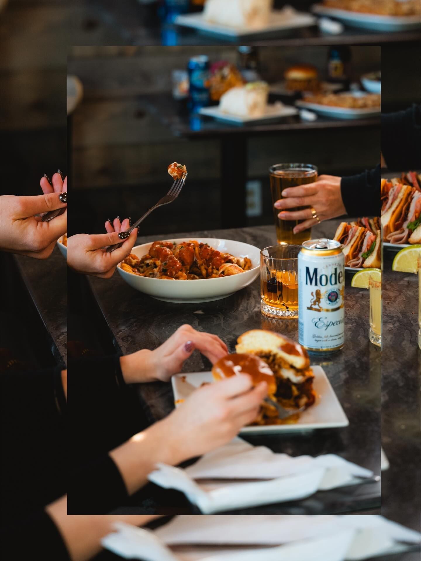 People eating a meal at a restaurant. A person holds a forkful of food, and another a sandwich. Beer and food on the table.