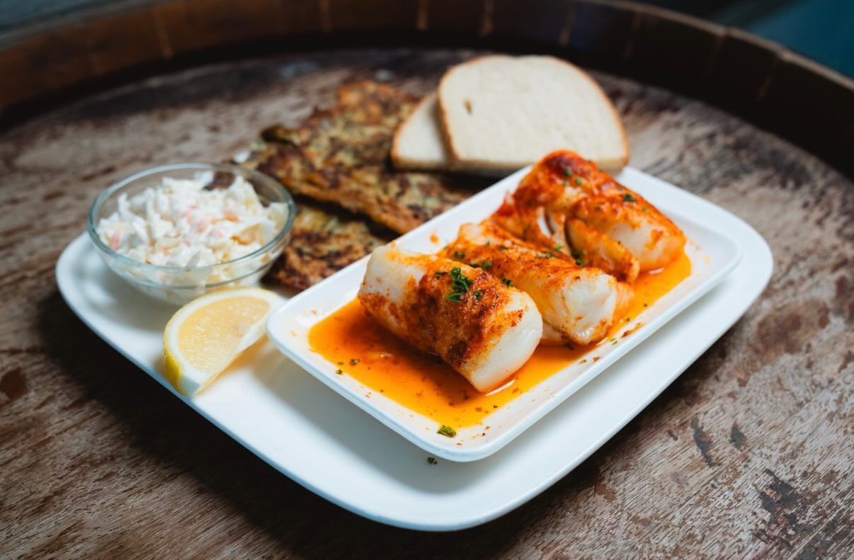 Plate of food with fish, coleslaw, crackers, bread, and lemon.