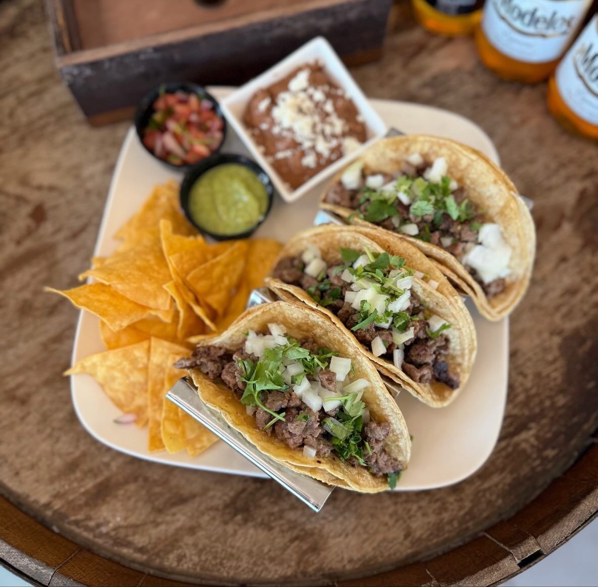 Plate of tacos with sides of salsa, refried beans, guacamole, and chips.
