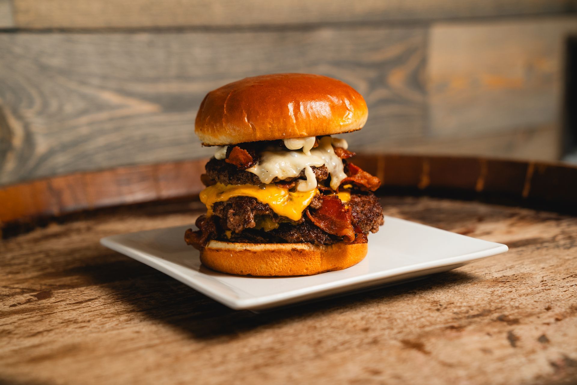 Double cheeseburger with bacon and sauce on a white plate atop a wooden surface.