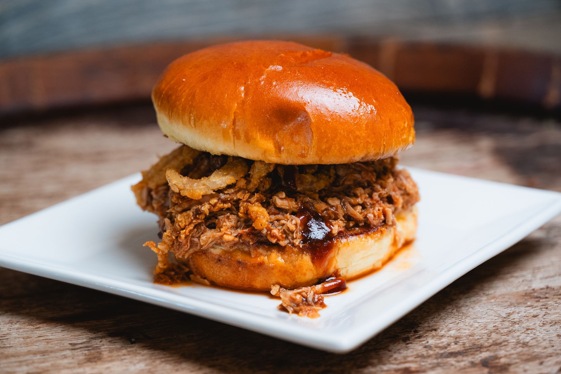 Pulled pork sandwich with crispy onion rings on a brioche bun, on a white plate.