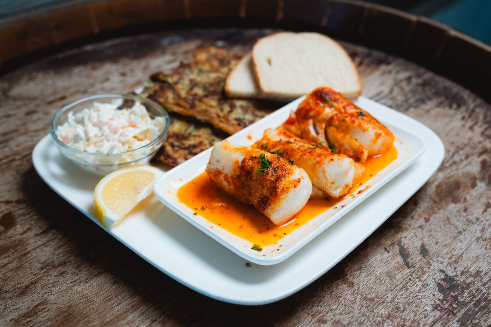 Seafood dish on a white plate with coleslaw, bread, and a lemon wedge on a wooden surface.
