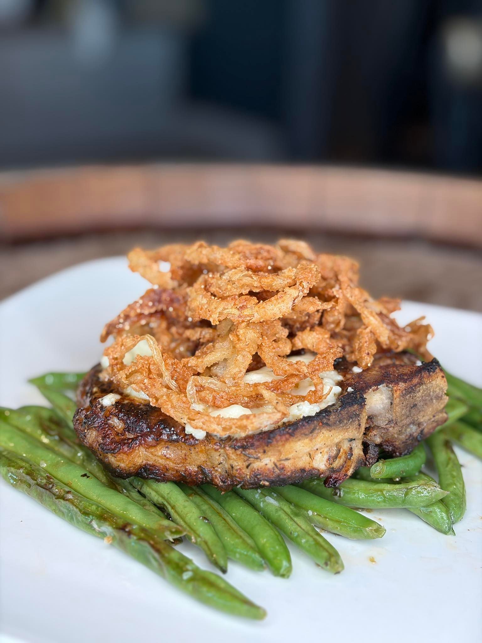 Pork chop with fried onions on a bed of green beans on a white plate.