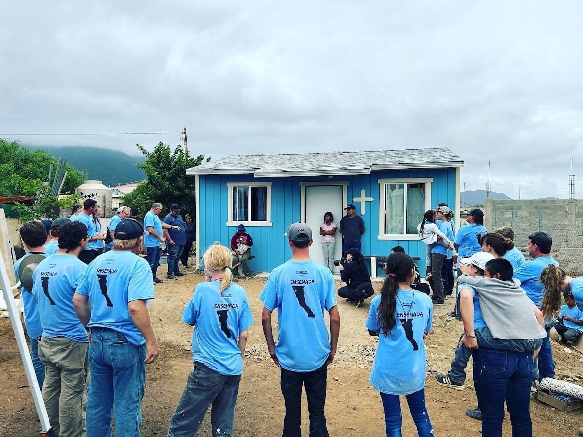 A group of people in blue shirts are standing in front of a blue house.