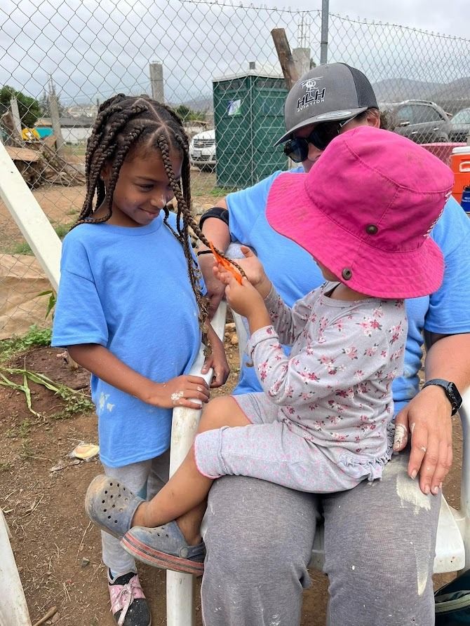 A man is sitting on a bench with two children . one of the children is wearing a pink hat.