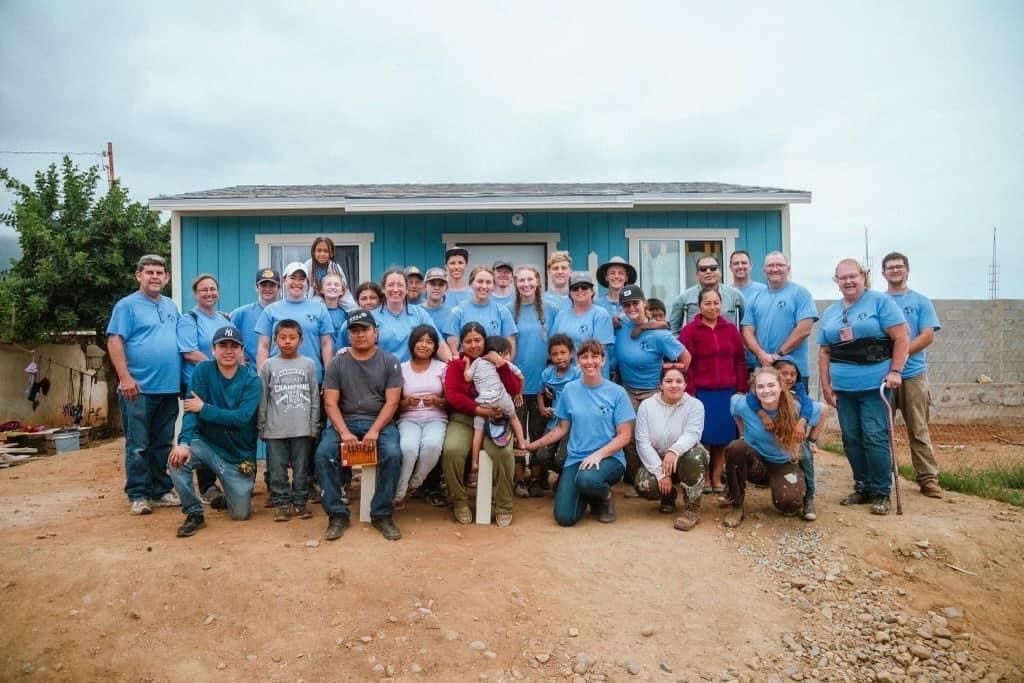 A group of people are posing for a picture in front of a blue house.
