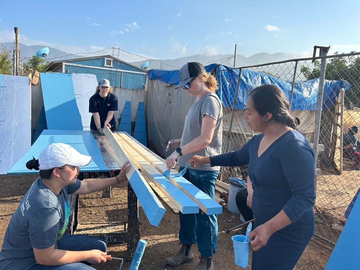 A group of women are painting a blue table outside.