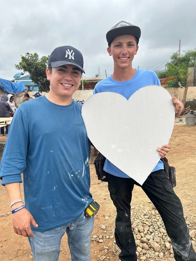 Two men standing next to each other holding a large white heart