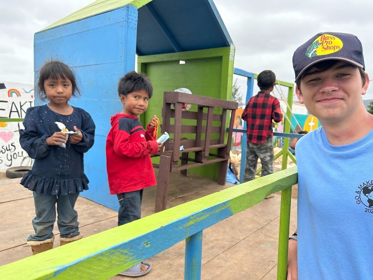 A man is standing next to two children in front of a playground.