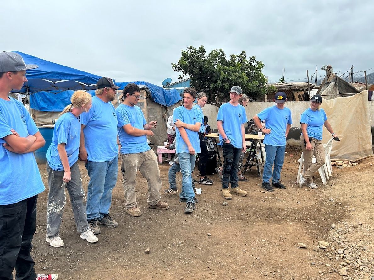 A group of people wearing blue shirts are standing in a dirt field.