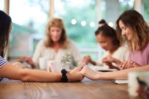 A group of women are sitting at a table holding hands and praying.