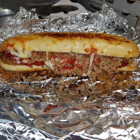 A cheesy stromboli sandwich is sitting on a piece of tin foil